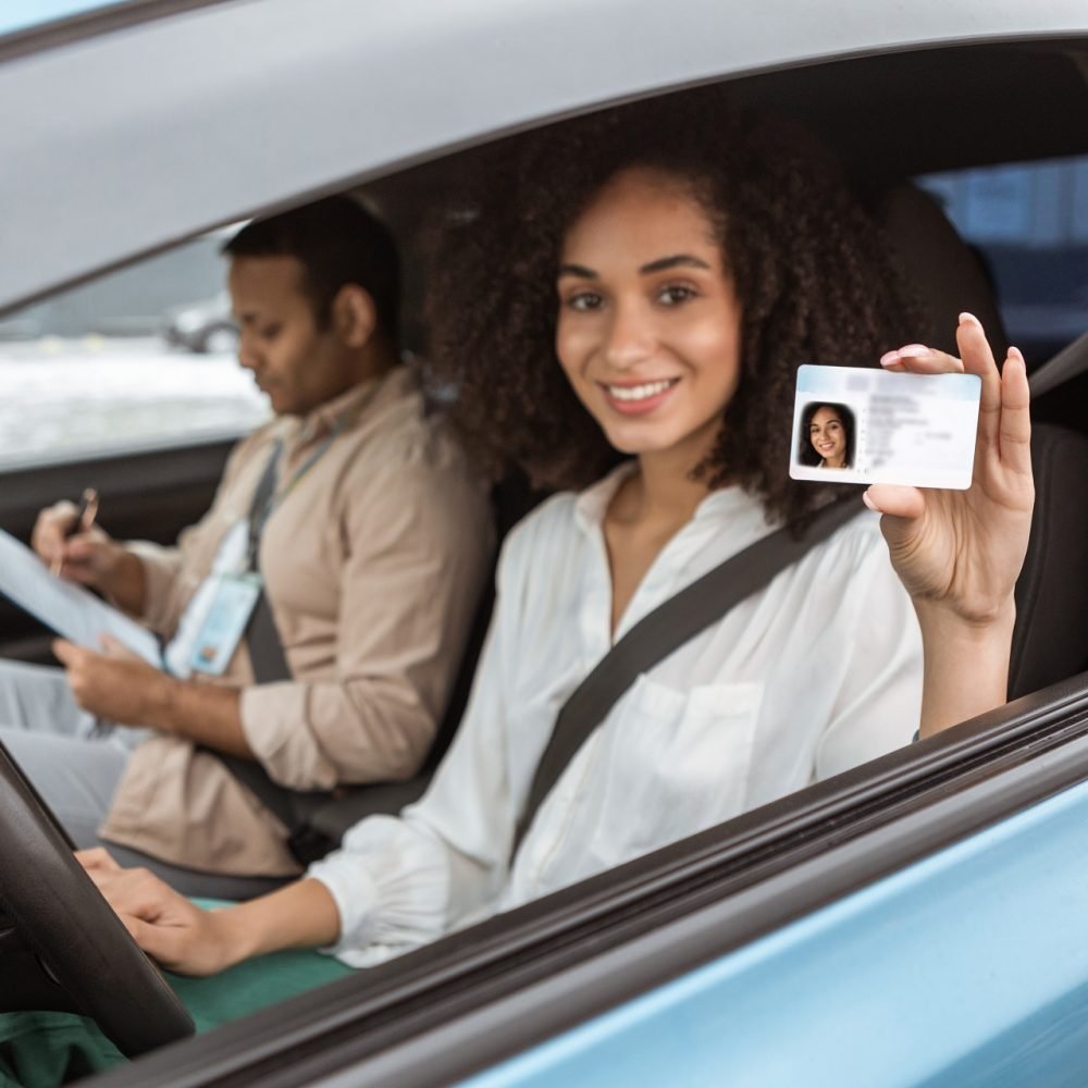 Cheerful Arabic Novice Driver Lady Showing Driving License Card Through Open Automobile Window, Sitting Beside Instructor Man In Car. Woman Got Her Driver's Permit Concept. Selective Focus